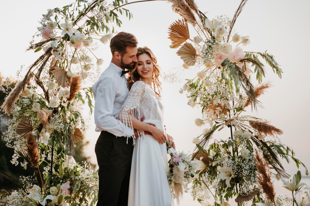 Bride and groom embracing under floral wedding arch.